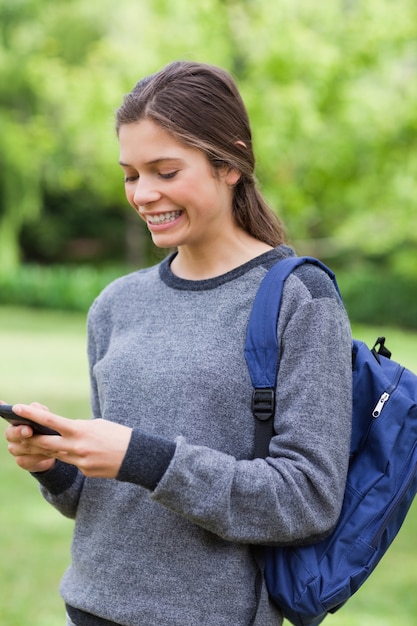 Glimlachend jong meisje dat een tekst met haar mobiele telefoon verzendt