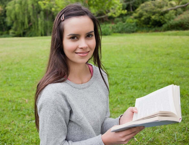 Glimlachend jong meisje dat zich rechtop in het platteland bevindt terwijl het lezen van een boek