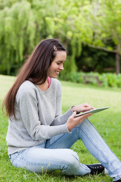 Glimlachend jong meisje die haar tabletpc met behulp van terwijl het zitten in een park