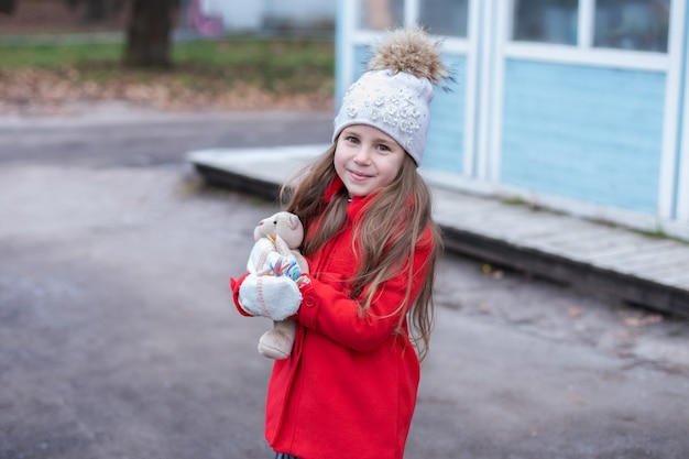 Glimlachend jong meisje in rode kapstok met teddybeer in handen op straat in kerstmis