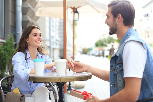 Glimlachend jong meisje met een date met haar vriendje in de coffeeshop, man met huidige doos.