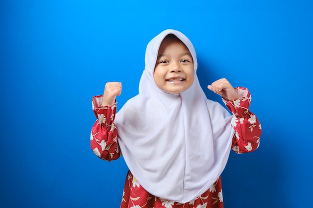 Glimlachend jong moslimmeisje in hijab rode kleren, op zoek naar camera geïsoleerd op blauwe muur achtergrond, studio portret. Mensen religieuze levensstijl concept.