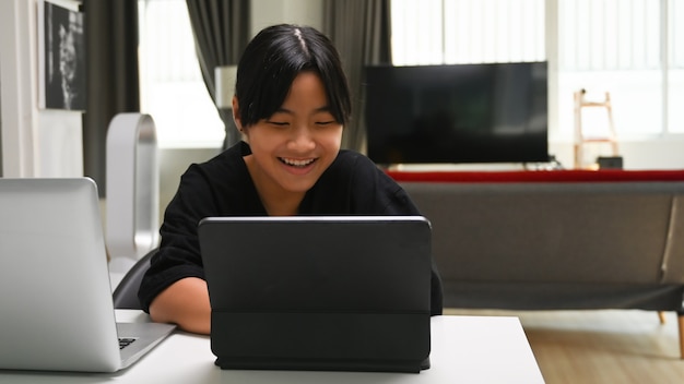 Glimlachend jong schoolmeisje dat thuis online studeert met tabletcomputer. Online onderwijsconcept.