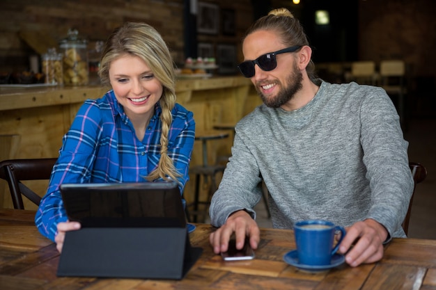 Glimlachend jong stel met behulp van tabletcomputer aan tafel in cafetaria