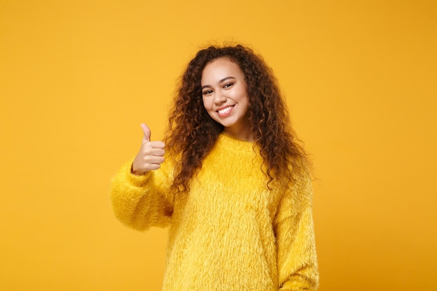 Glimlachend jonge Afro-Amerikaanse meisje in bont trui poseren geïsoleerd op geel oranje muur achtergrond, studio portret. Mensen oprechte emoties levensstijl concept. Bespotten kopie ruimte. Duim omhoog laten zien.