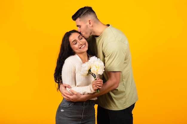 Glimlachend jonge arabische man kussende knuffelende vrouw met boeket bloemen gefeliciteerd met verjaardag