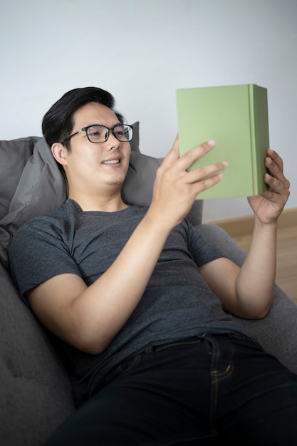 Glimlachend jonge aziatische man leesboek op de bank.