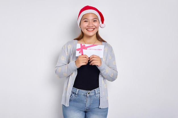 Glimlachend jonge Aziatische vrouw 20s in hoed Kerstmis ontvangt en toont een cadeaubon coupon voucher kaart geïsoleerd op witte studio achtergrond Merry Christmas Concept