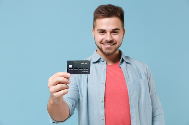 Glimlachend jonge, bebaarde man 20s in casual shirt poseren geïsoleerd op pastel blauwe muur achtergrond studio portret. Mensen oprechte emoties levensstijl concept. Bespotten kopie ruimte. Houd creditcard bankpas.
