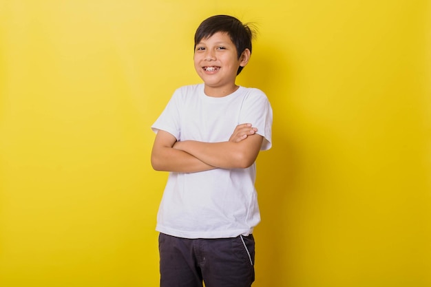 Glimlachend jongetje kruist zijn armen geïsoleerd op gele achtergrond