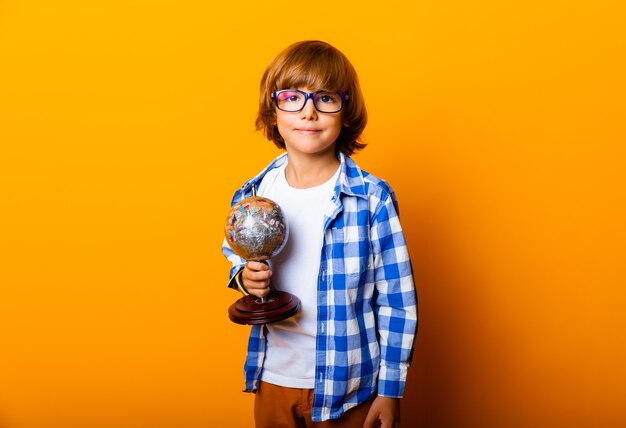 Glimlachend jongetje met een bril van 7 jaar oud, met een wereldbol op een gele achtergrond, studioportret van een kind onderwijs concept