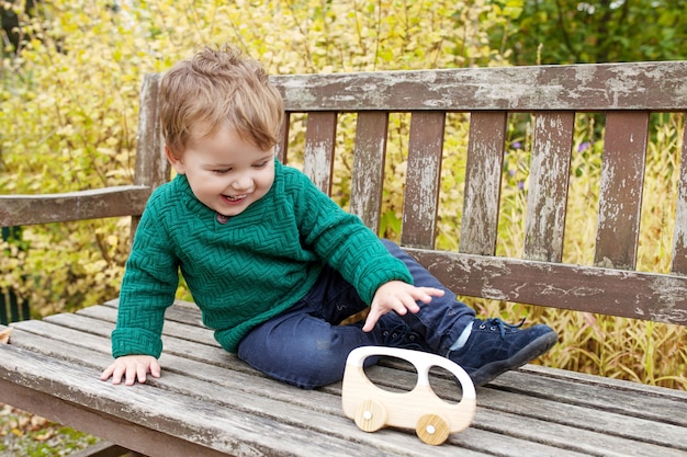 Glimlachend jongetje wandelen in het park. Mooie kleine jongen spelen met houten auto buiten.