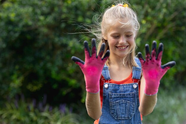 Foto glimlachend kaukasisch meisje in de tuin die handen omhoog houdt en vuile roze tuinhandschoenen draagt