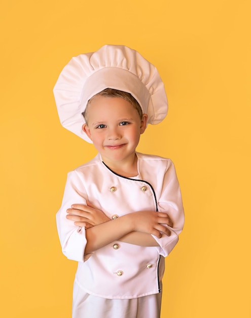 Glimlachend kind in wit chef-kokuniform met een grappige hoed Vrolijke gele achtergrond