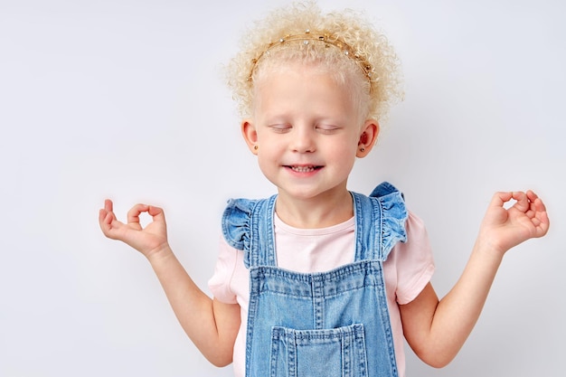 Glimlachend kind meisje mediteren geïsoleerd op witte studio achtergrond schattige blanke jongen in jurk poseren...