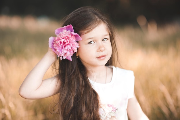 Glimlachend kind meisje met bloem pioenroos in haar buitenshuis Lente