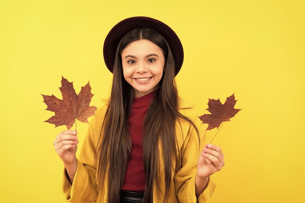 Glimlachend kind met plezier met esdoornblad op gele achtergrond herfst natuur