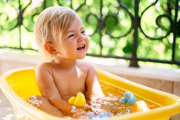 Glimlachend kind zit in een kom met water en speelgoed op het balkon