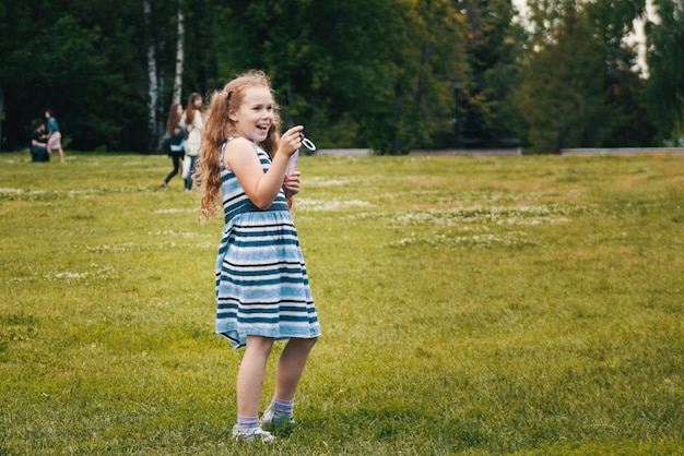 Glimlachend kindmeisje dat blauwe zomerjurk draagt, speelt in het park, buitenportret