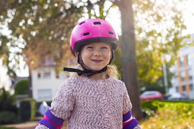 Glimlachend kindmeisje in een helm in beschermingsrolschaatsen in het park