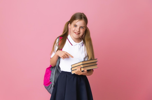 Glimlachend klein blond meisje 1012 jaar oud in schooluniform met rugzak met boeken geïsoleerd op pastelroze achtergrond studioportret Het concept van kinderlevensstijl Onderwijs op school