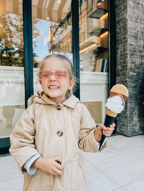 Foto glimlachend klein meisje met een grote ijshoorn in haar hand staat bij het gebouw op straat