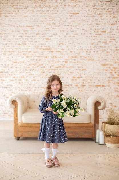 glimlachend klein meisje met krullend haar met een boeket jasmijnbloemen in de woonkamer kind met een boeket bloemen voor mama