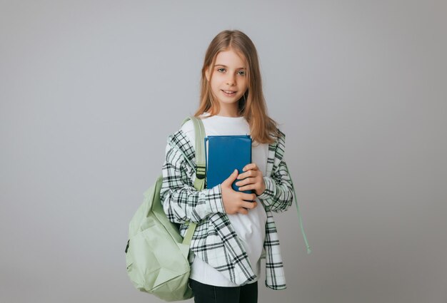 Glimlachend klein schoolmeisje 1113 jaar oud met rugzak met boek geïsoleerd op grijze achtergrond studio portret Het concept van kinderlevensstijl Onderwijs op school