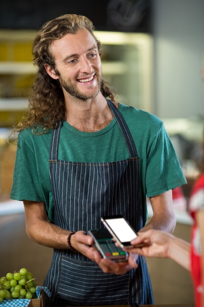 Glimlachend mannelijk personeel dat een betaling ontvangt via nfc-technologie aan de balie