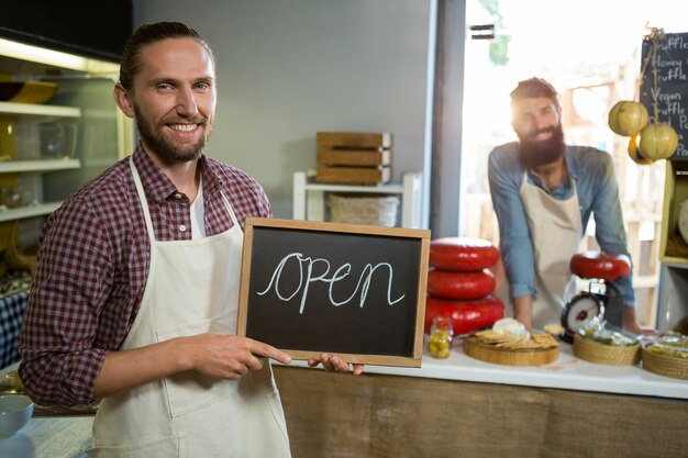 Glimlachend mannelijk personeel dat een open teken houdt