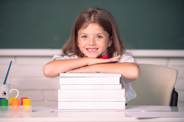 Glimlachend meisje dat aan de balie zit en handen vasthoudt aan de boeken in het klaslokaal van de school Educatief proces