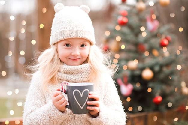 Glimlachend meisje dat buiten thee drinkt boven de kerstboom