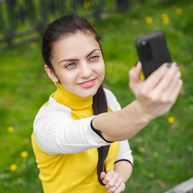 Glimlachend meisje dat foto met smartphonecamera buiten neemt. selfie