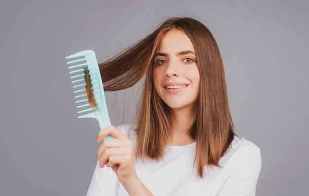 Glimlachend meisje dat haar kamt, mooie jonge vrouw met kam rechtgetrokken haar aantrekkelijke glimlachende vrouw