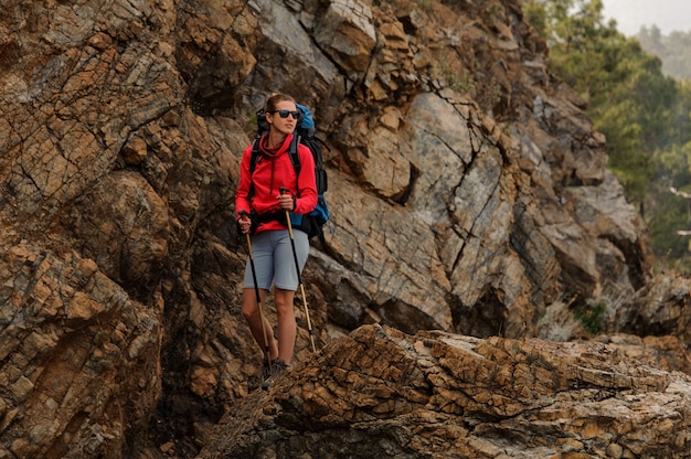 Glimlachend meisje dat zich op de rotsen met wandelingsrugzak en wandelstokken bevindt