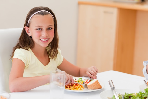 Glimlachend meisje die diner hebben bij dinerlijst