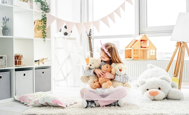 Glimlachend meisje die teddyberen koesteren die op vloer binnen zitten