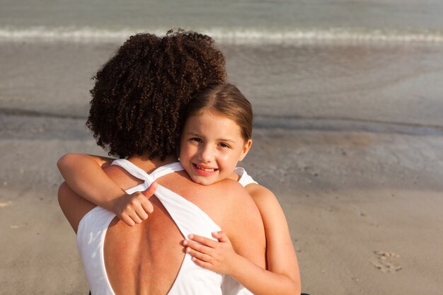 Glimlachend meisje en haar moeder die een omhelzing op het strand hebben