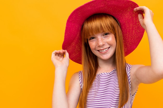 Glimlachend meisje in een de zomer rode hoed over geel