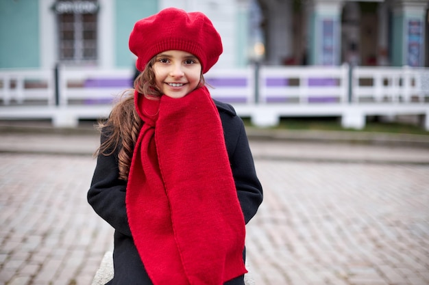 Glimlachend meisje in een rode baret en jas op een stadsstraat. Hoge kwaliteit foto