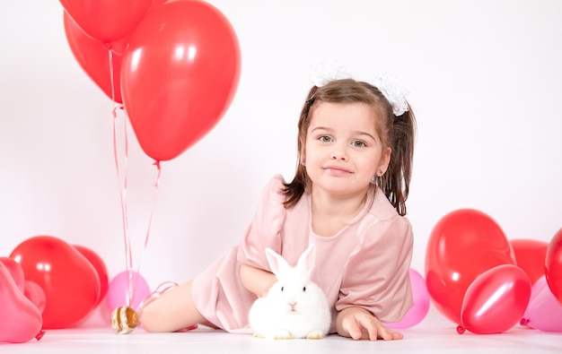 Glimlachend meisje in een roze t-shirt met haar kleine witte konijn en rode ballonnen cadeau gelukkig kind