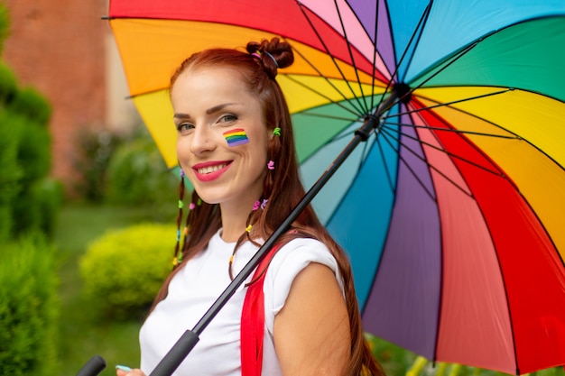 Glimlachend meisje in kleurrijke kleren en lgbt-vlag bij haar die in openlucht stellen.