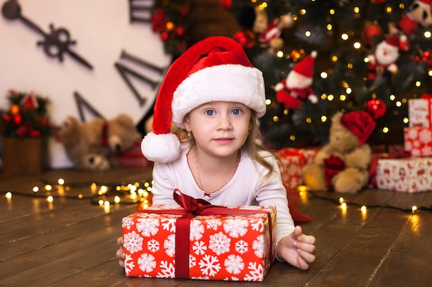 Glimlachend meisje in rode pyjama's en de doos van de de holdingsgift van de Kerstmanhoed