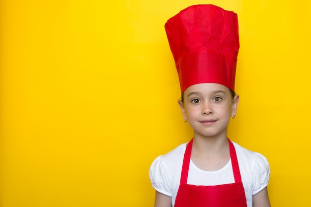 Glimlachend meisje in rood chef-kokkostuum op geel