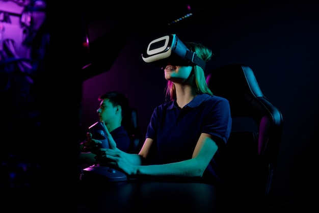 Glimlachend meisje in virtual reality-bril, zittend in de leunstoel van gamers en het gebruik van joystickgreep tijdens het spelen van videogame in computerclub