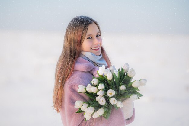 Glimlachend meisje in winterkleding met een boeket witte tulpen tegen een besneeuwd landschap
