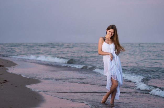 Glimlachend meisje in witte jurk poseren voor foto op het strand