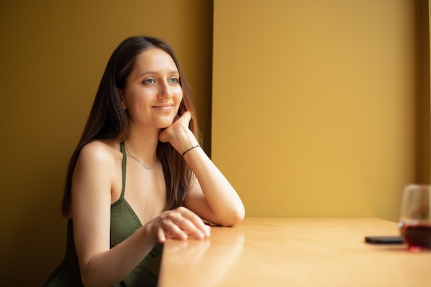 Glimlachend meisje kijkt uit het raam terwijl ze aan een tafel zit in een café tegen de achtergrond van een gele muur