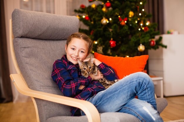 Glimlachend meisje knuffelt haar nieuwe kat in de buurt van de kerstboom thuis