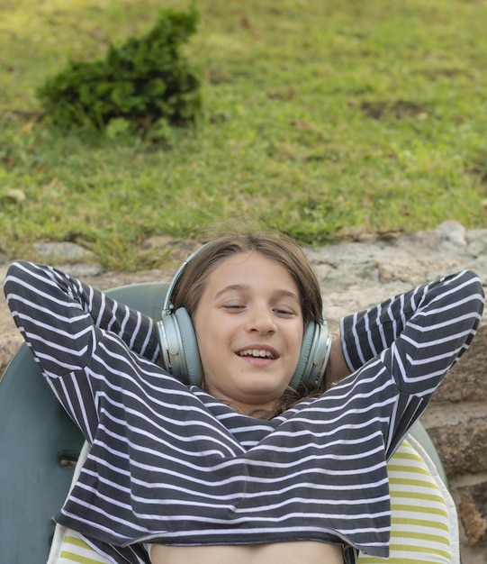 Glimlachend meisje liggend met haar handen in haar nek luisterend naar muziek met draadloze hoofdtelefoons